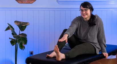 Elyse Newland smiling while reaching for her left foot on a therapy bench