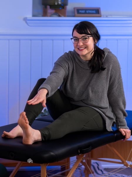 Elyse Newland sitting on a therapy bench reaching for her left toe